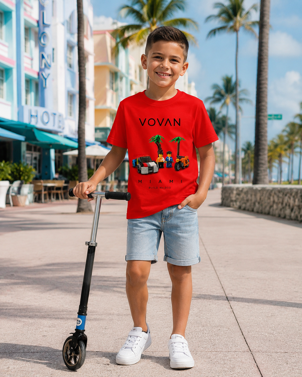 Child wearing a red 'VOVAN MIAMI BUILD 003' t-shirt with a scooter on a city street.